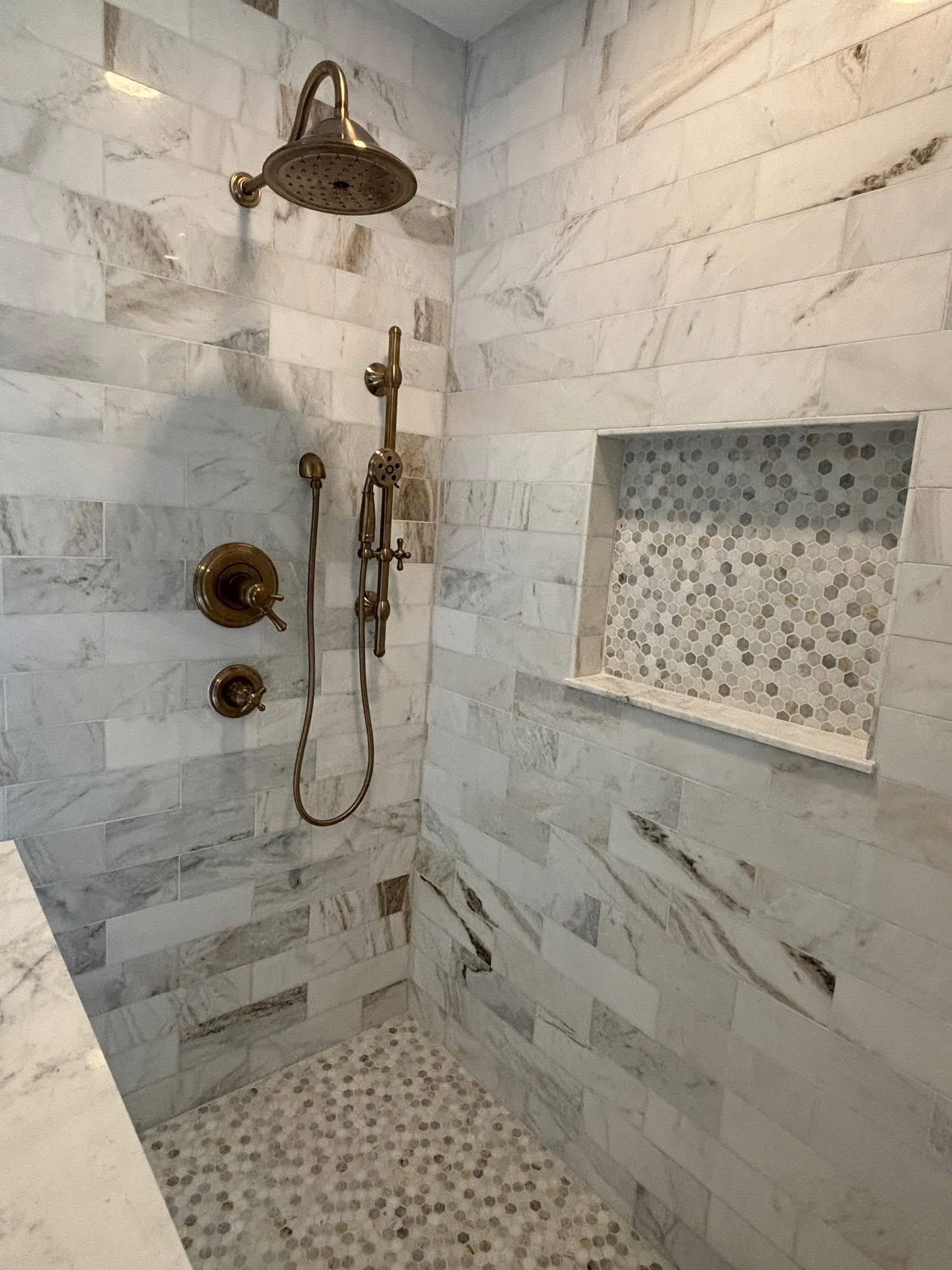 Marble shower with bronze fixtures and hexagon mosaic niche